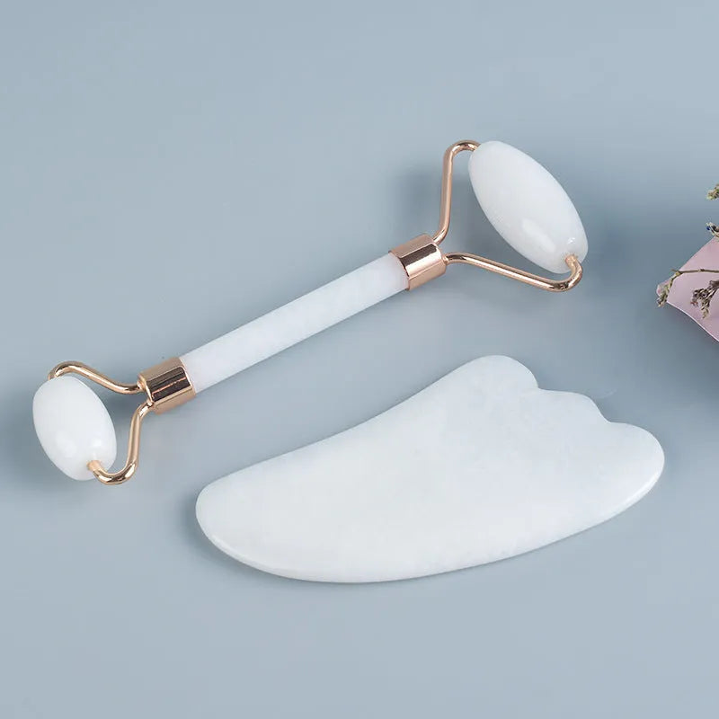 White jade facial roller with double heads and matching scraping board on dark surface