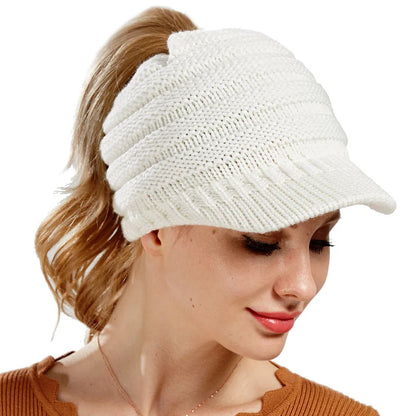 Woman wearing a light grey knitted ponytail beanie with her ponytail pulled through the hole in the back.