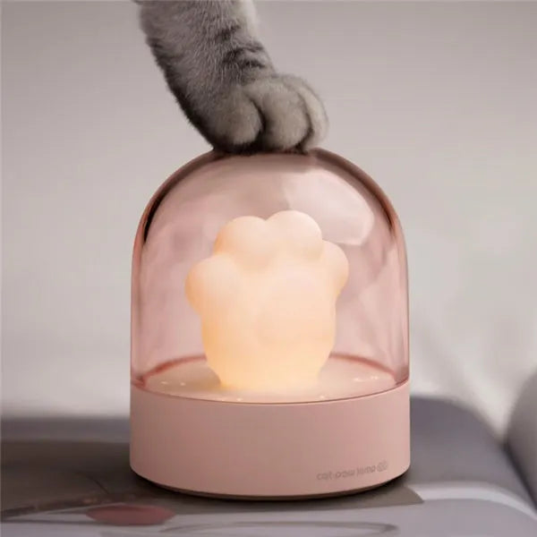 Grey cat paw shaped night light with USB port and button, glowing softly on a wooden desk.