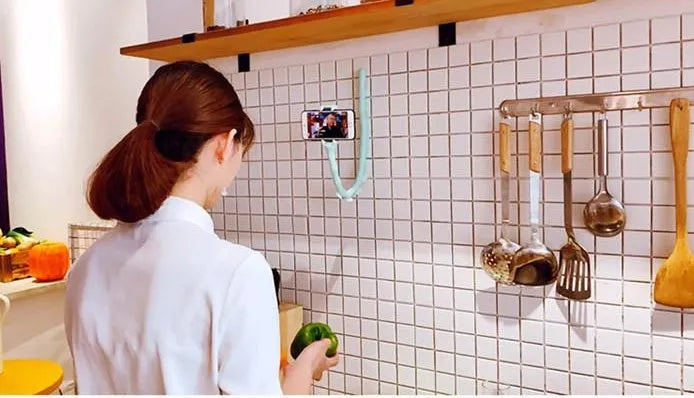 Black flexible gooseneck phone holder with suction cup mounted on a desk, holding a mobile phone at an angle.