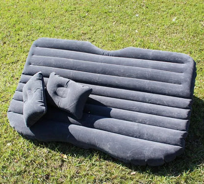 Black inflatable car bed with flocked surface and two pillows, shown folded into a chair inside a vehicle.