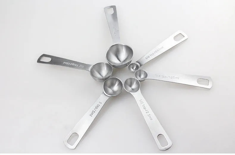 Six stainless steel measuring spoons with engraved markings and D-shape ring, sizes 1/8 tsp to 1 Tbsp