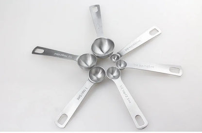 Six stainless steel measuring spoons with engraved markings and D-shape ring, sizes 1/8 tsp to 1 Tbsp