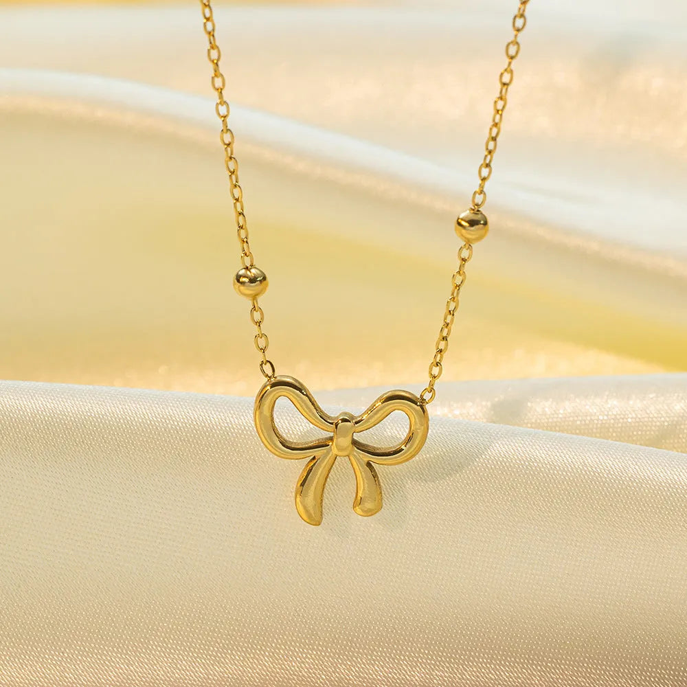 Gold electroplated bow pendant on an adjustable titanium steel cross chain necklace for women.