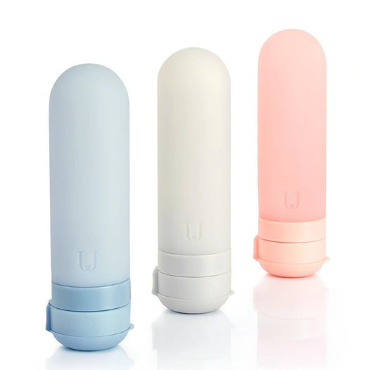 Set of three silicone travel bottles in light grey, pink, and blue colours with screw caps