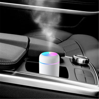 Pink car air purifying humidifier with LED lights on, next to a USB cable.