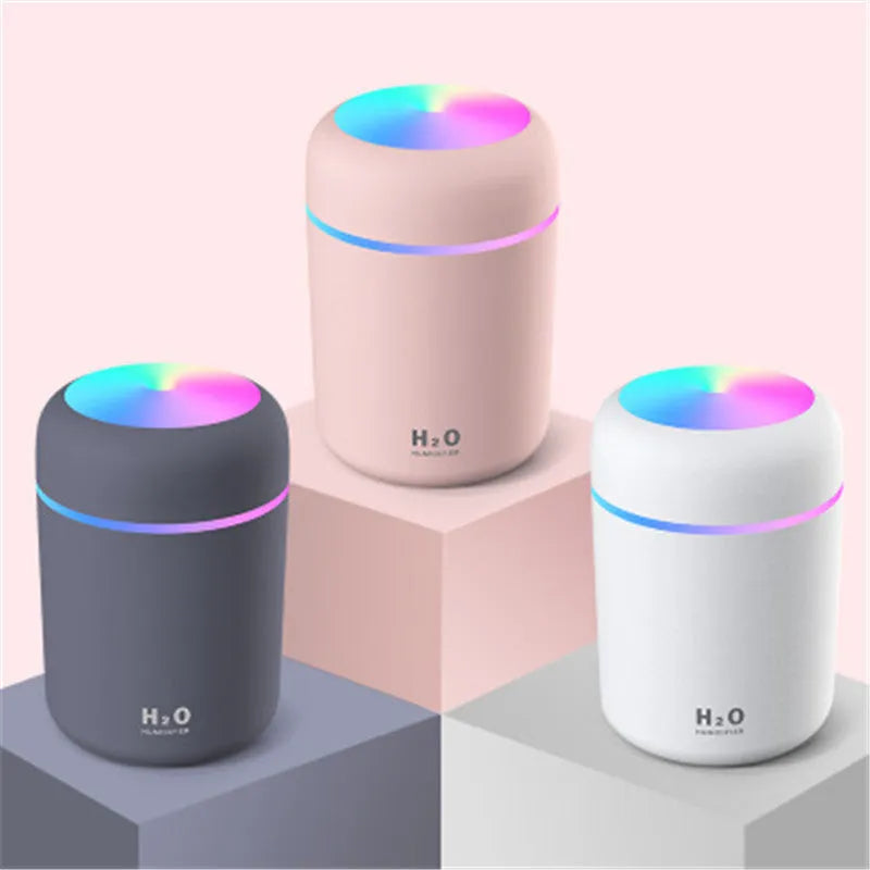 Pink car air purifying humidifier with LED lights on, next to a USB cable.