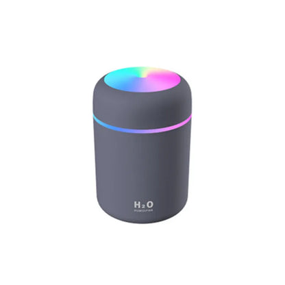 Pink car air purifying humidifier with LED lights on, next to a USB cable.