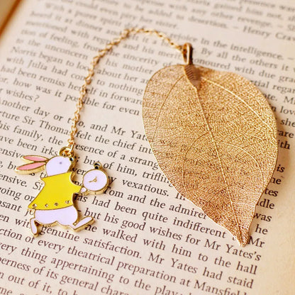 KC alloy metal bookmark with leaf, Alice, rabbit, and clock charms on an open book.