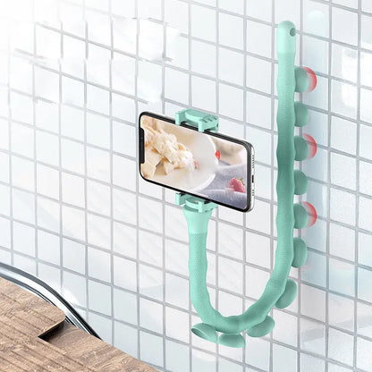 Black flexible gooseneck phone holder with suction cup mounted on a desk, holding a mobile phone at an angle.