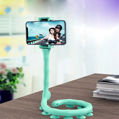 Black flexible gooseneck phone holder with suction cup mounted on a desk, holding a mobile phone at an angle.