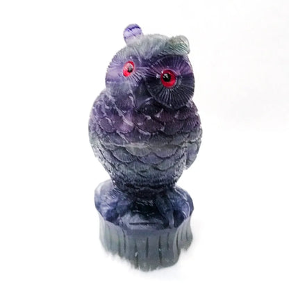 Hand-carved purple fluorite stone owl ornament on a neutral background, showing detailed carving.