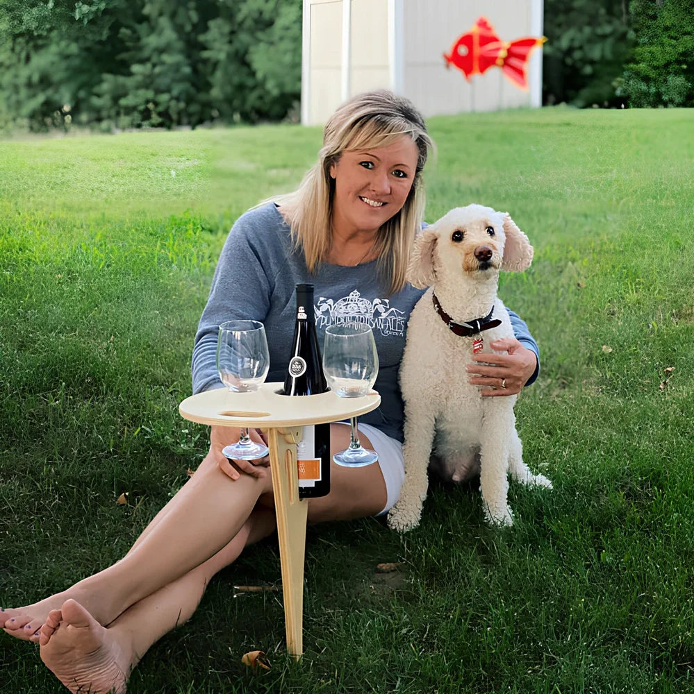 Wooden folding wine table with ground stakes holding wine bottle and glasses outdoors