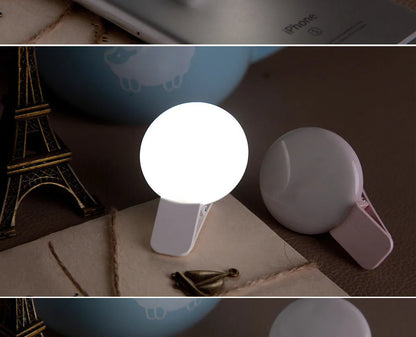 Round black mobile phone fill light with adjustable clip attached to a smartphone.