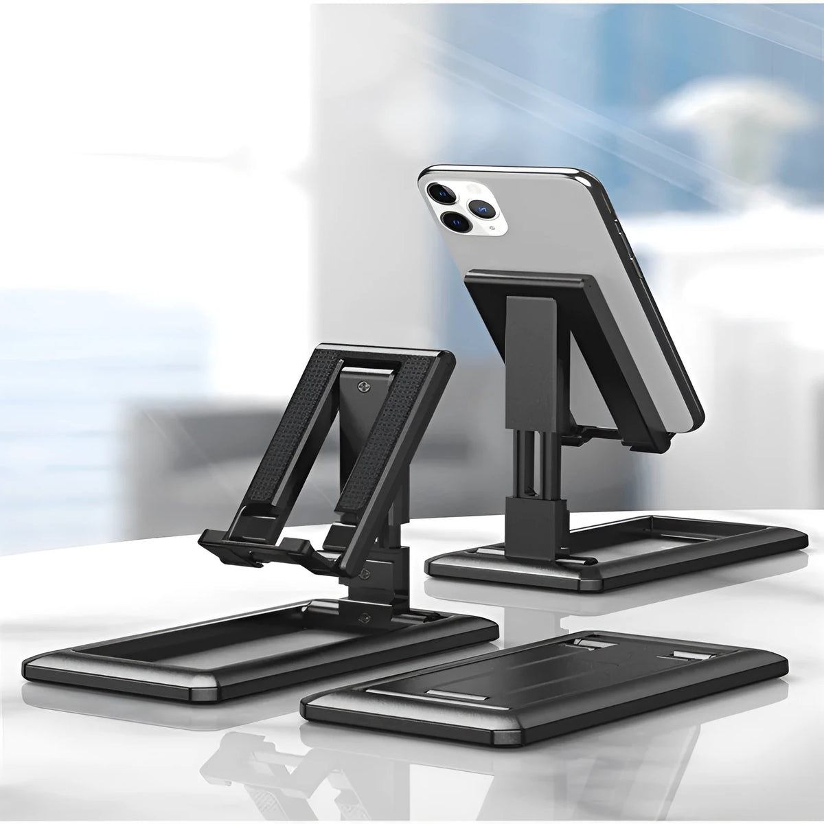 Retractable folding mobile phone stand in an adjusted position on a desktop, shown in one of four colour options.