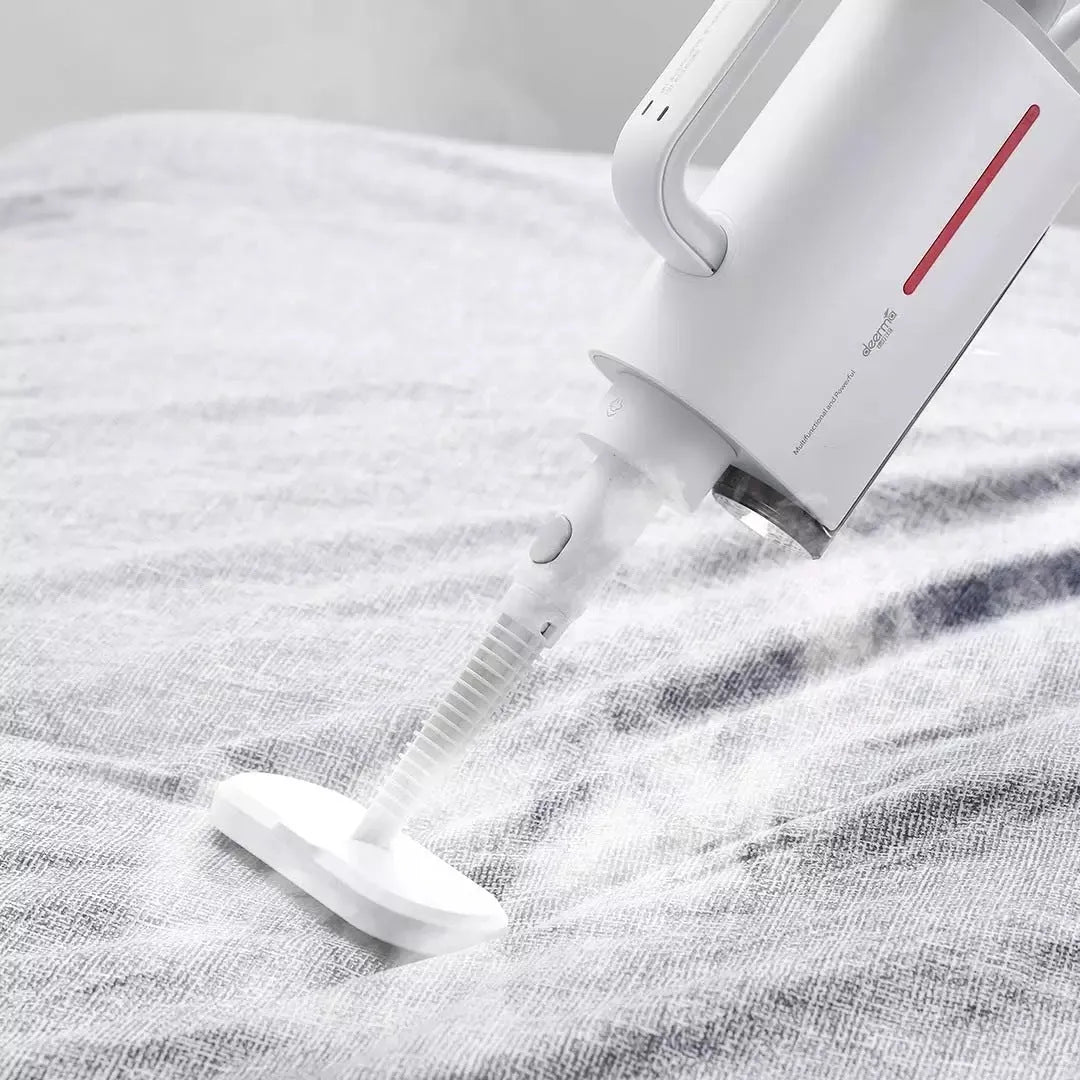 White Deerma handheld steam cleaner with multiple brush heads and extension tubes on a table