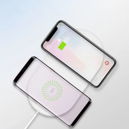 White dual wireless fast charging pad for two mobile phones on a wooden desk.
