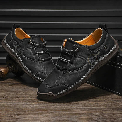 Men's plain black casual leather shoes with round toe and microfiber upper on a wooden floor.