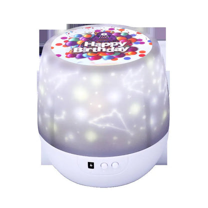 Compact white starry sky projector lamp with Bluetooth speaker projecting constellation images on a blue wall.