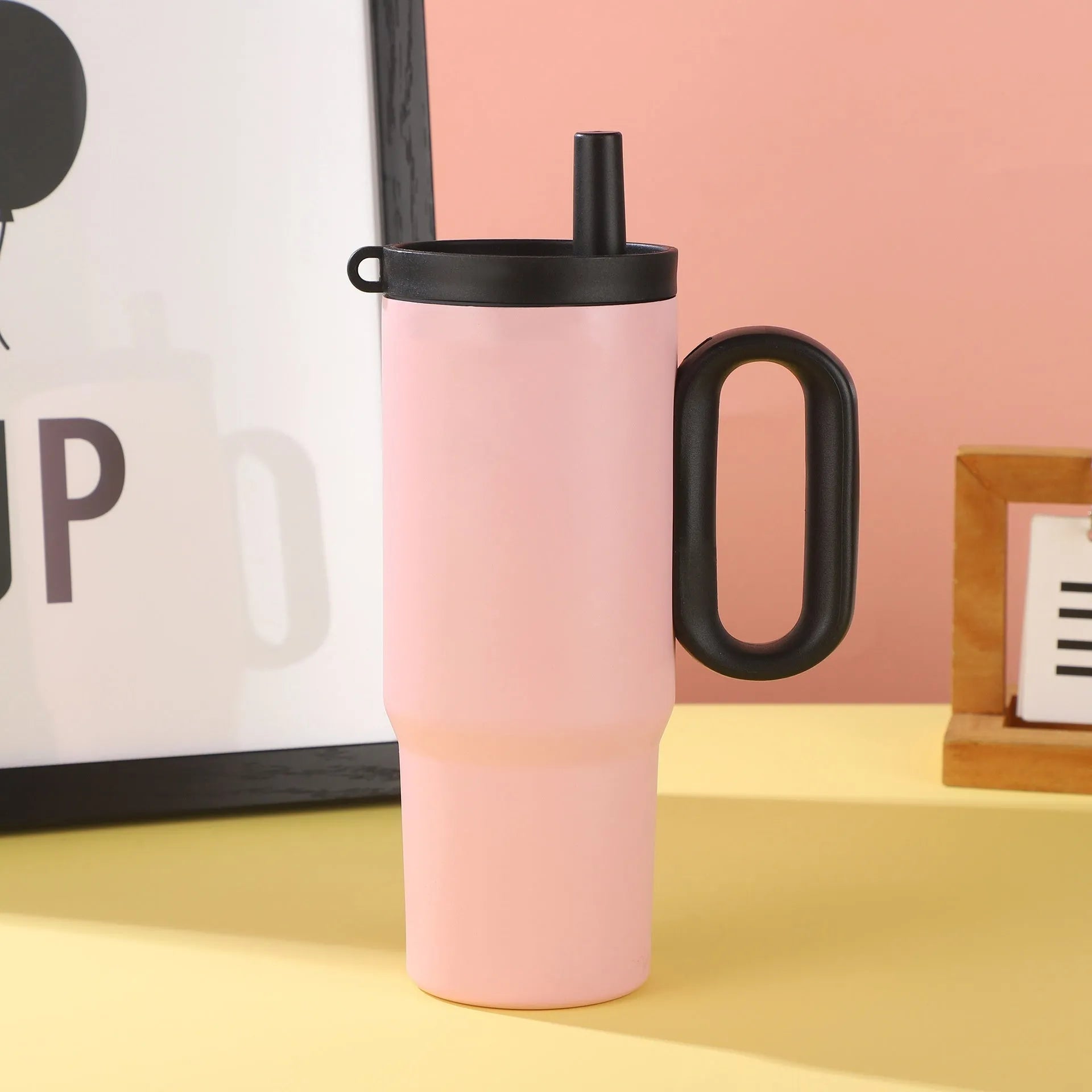 Large pink insulated straw cup with a black handle and push-button lid on a wooden table