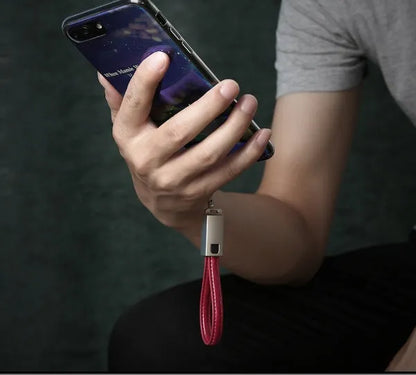 Short black leather iPhone charging cable with metal connector next to a power bank