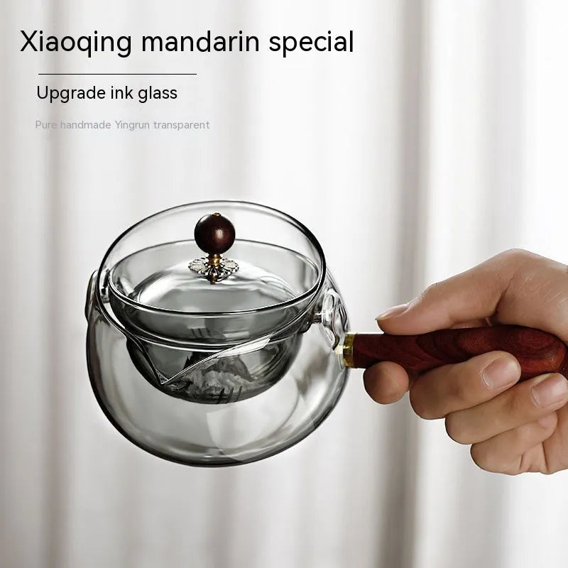 Glass teapot with wooden handle showing transparent borosilicate construction and removable infuser