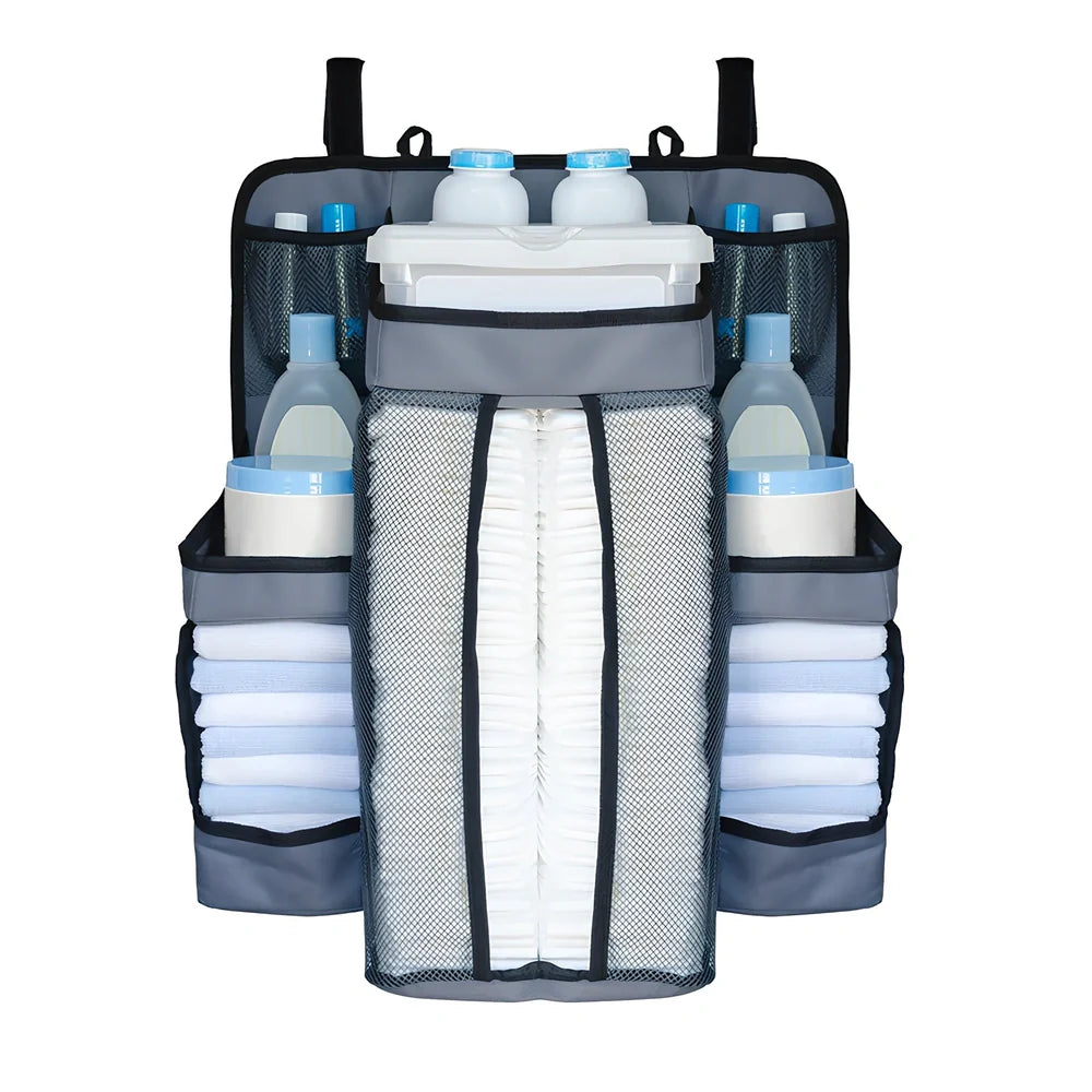 Grey baby nappy organiser attached to crib rail with Velcro straps, showing storage compartments for nappies and essentials