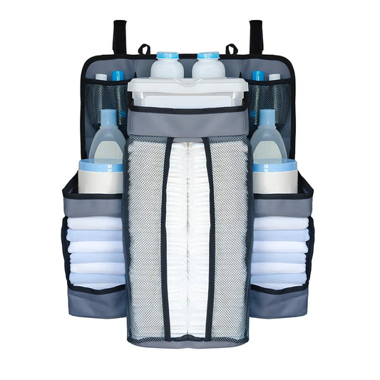 Grey baby nappy organiser attached to crib rail with Velcro straps, showing storage compartments for nappies and essentials
