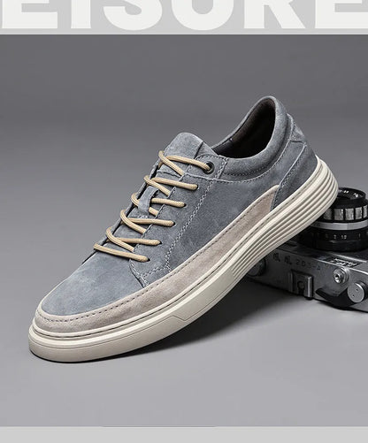 Men's grey low-top casual leather skate shoes with round toe and flat rubber sole on a wooden surface.