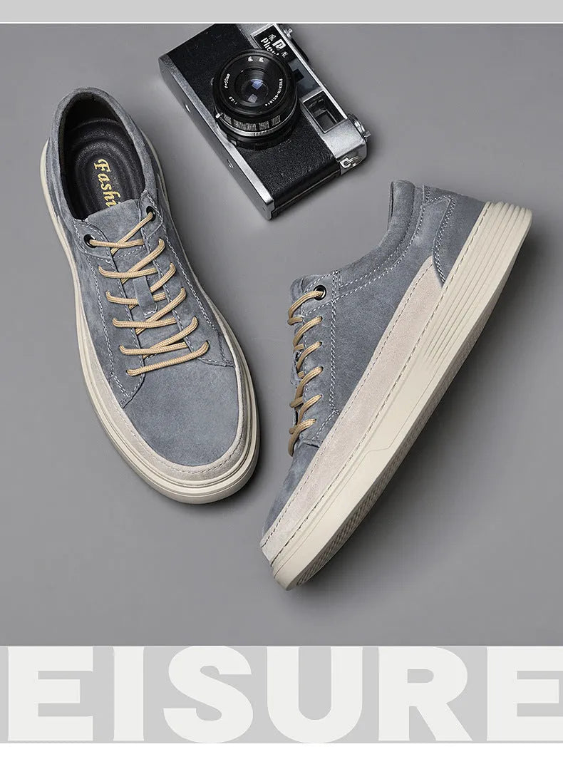 Men's grey low-top casual leather skate shoes with round toe and flat rubber sole on a wooden surface.