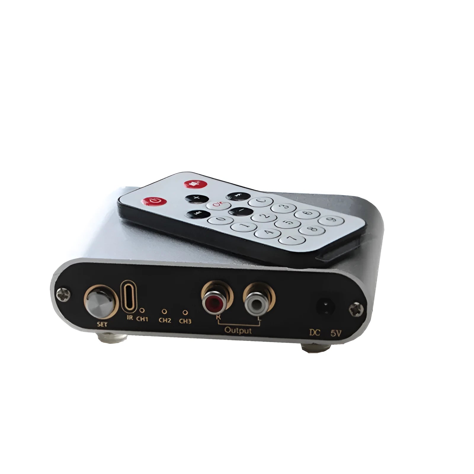 Silver aluminium audio source switch selector unit with infrared remote control on a black surface.