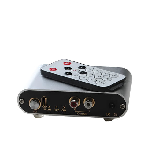 Silver aluminium audio source switch selector unit with infrared remote control on a black surface.