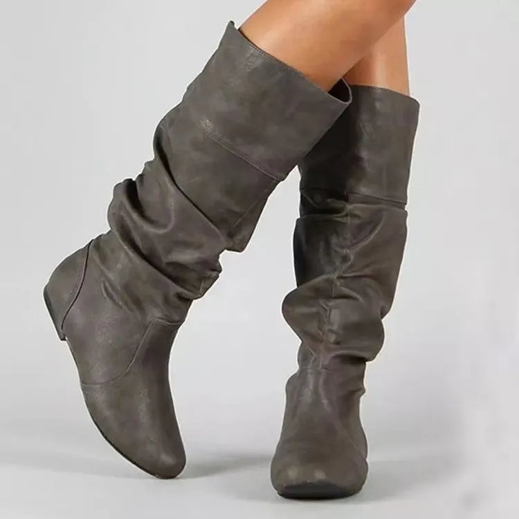 Women's flat slip-on boots in black with round toe and high cylinder shaft on a neutral background.