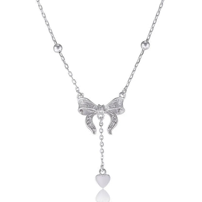 Close-up of a silver heart and bow pendant on an adjustable O-ring chain, resting on a collarbone.
