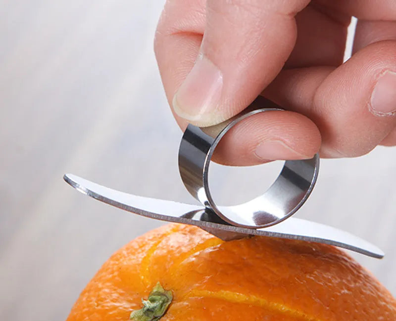 Silver stainless steel citrus fruit peeler with a ring handle on a wooden surface.