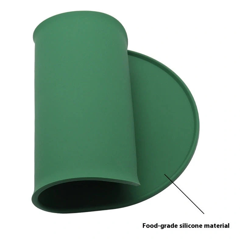 Green silicone cat feeding placemat with raised edges on wooden floor containing water bowl