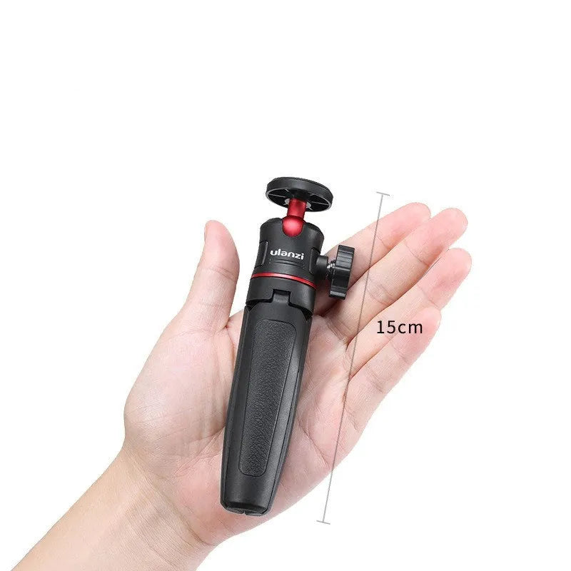 Compact black red and white phone tripod selfie stick stand extended next to a mobile phone.