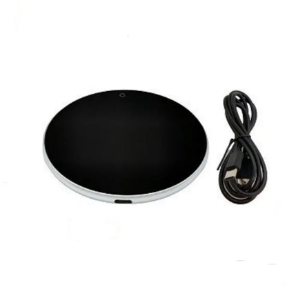 Black USB heating coaster on a desk next to a coffee mug, showing touch controls and coloured indicator light.