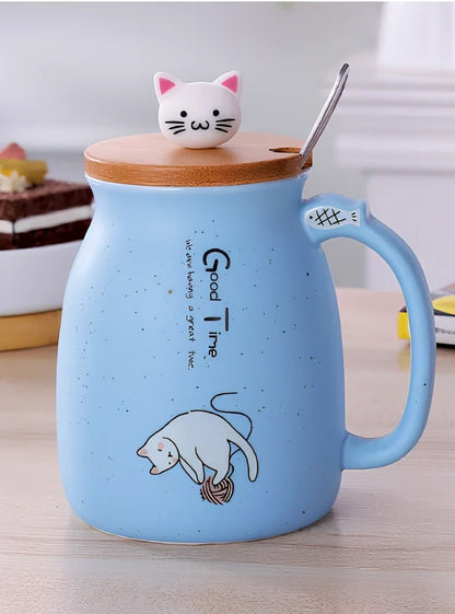 Pink ceramic mug with cartoon cat design, wooden lid, and stainless steel spoon on table