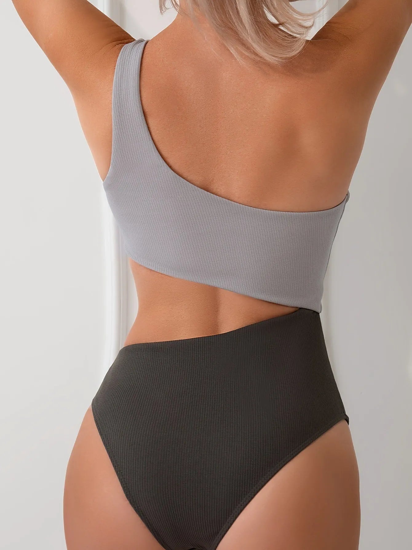 Women's light grey one-shoulder one-piece swimsuit made from polyester fabric.
