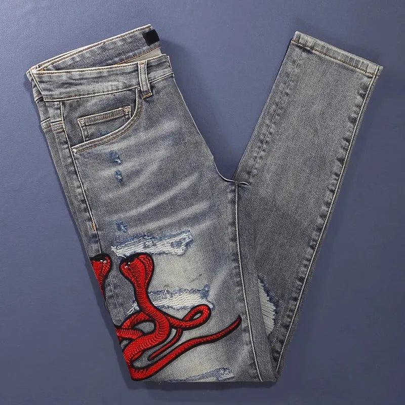 Men's slim fit blue jeans with washed-out finish, hole patches, and embroidery detail.