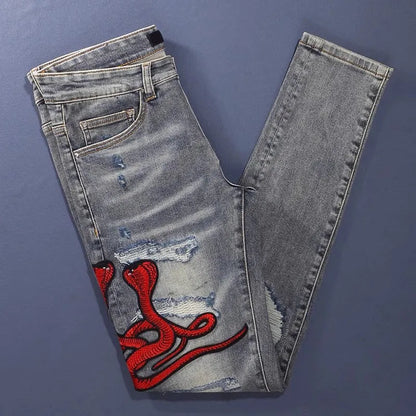 Men's slim fit blue jeans with washed-out finish, hole patches, and embroidery detail.