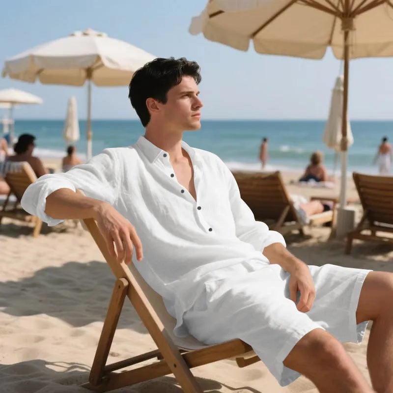 A man wearing a light blue linen long sleeve shirt and matching shorts on the beach.