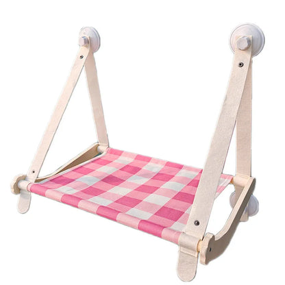Pink cat hammock with wooden frame and suction cups attached to a window, with a cat resting inside.