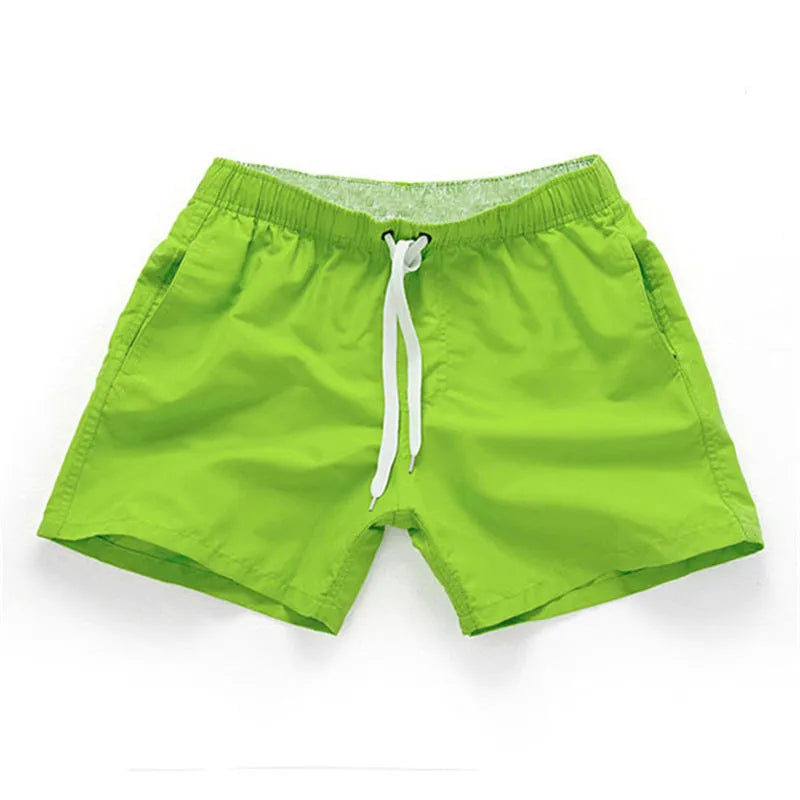 Man wearing straight-leg polyester beach shorts in a bright colour on the sand.