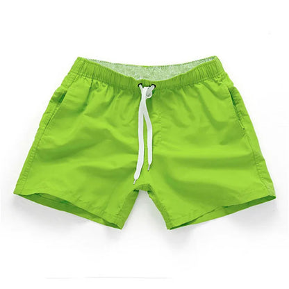 Man wearing straight-leg polyester beach shorts in a bright colour on the sand.