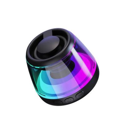 Small white portable Bluetooth speaker with LED light glow on a wooden desk next to a smartphone.