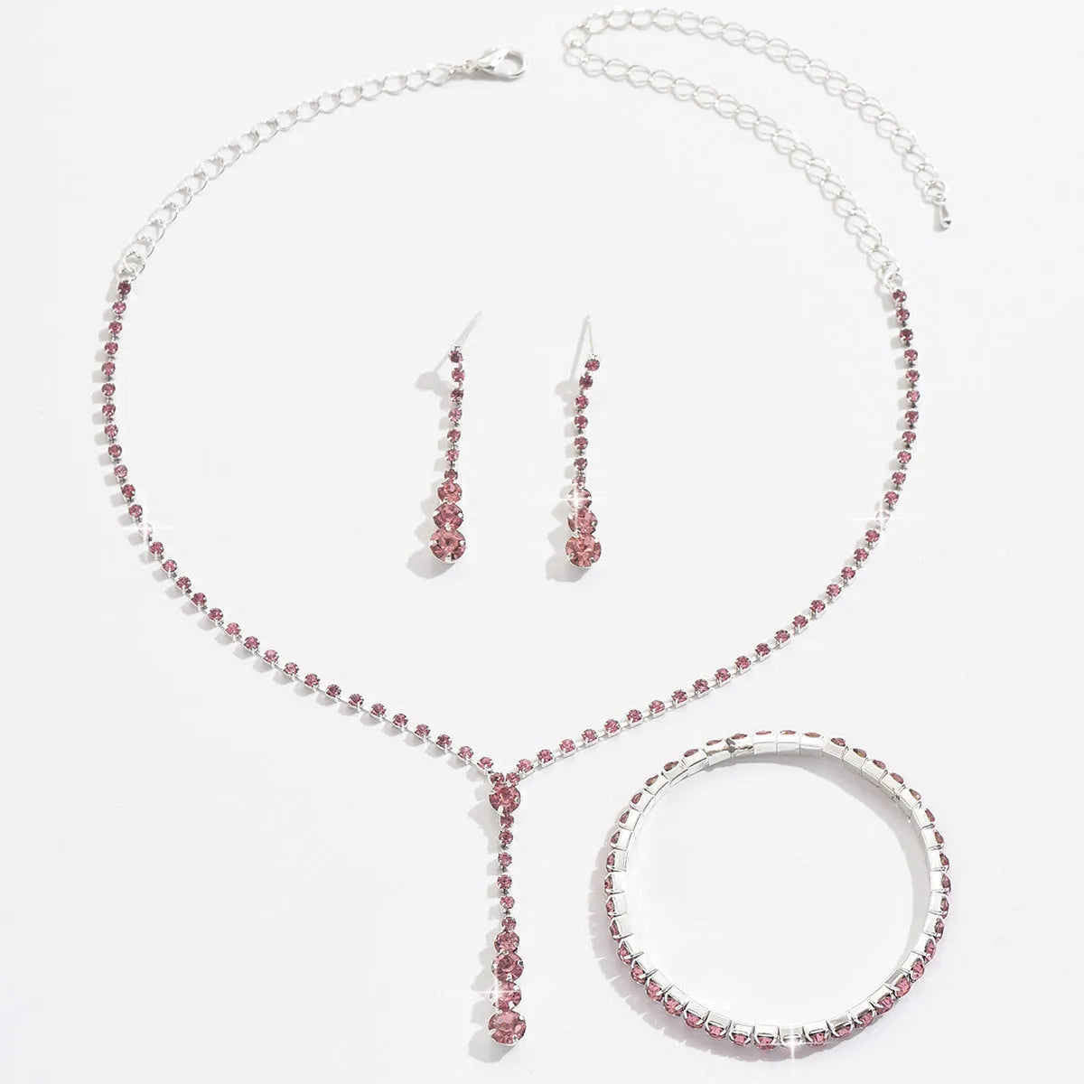 Women's silver pink rhinestone heart tassel earrings, necklace, and bracelet jewellery set on a white background.