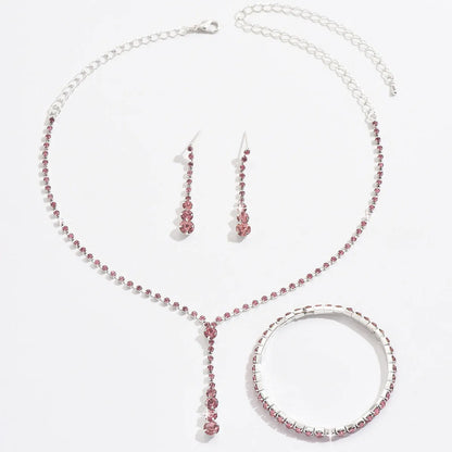 Women's silver pink rhinestone heart tassel earrings, necklace, and bracelet jewellery set on a white background.