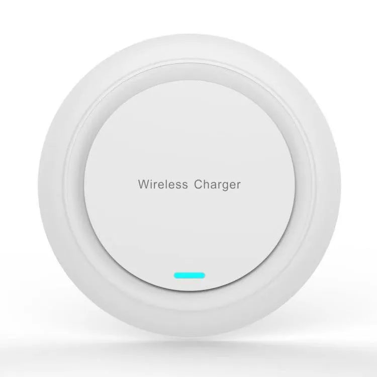 Round white wireless charging pad on desk next to mobile phone